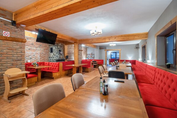 Un restaurante con mesas de madera, asientos tapizados en rojo y una pared de piedra, además de un televisor de pantalla plana montado en la pared.
