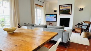 Un salon moderne avec une table à manger en bois, des chaises blanches, un canapé gris et un téléviseur.