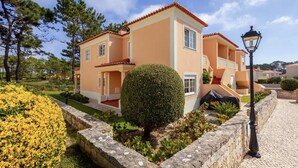 Un bâtiment à deux étages, surmonté d’un toit recouvert de tuiles rouges, avec un petit jardin agrémenté d’un arbuste aux allures soignées et un chemin pavé.