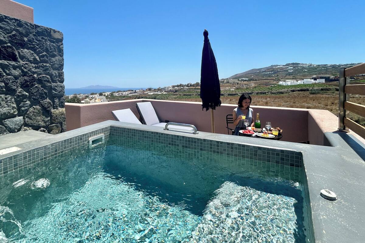 Área da piscina com água cristalina, mesa com comida e bebidas, e vista para a paisagem.