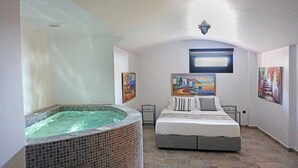 A bedroom with a large bed, a hot tub, and artwork on the walls. -  Golden Moments Luxury Stone Villas. (Santorini)