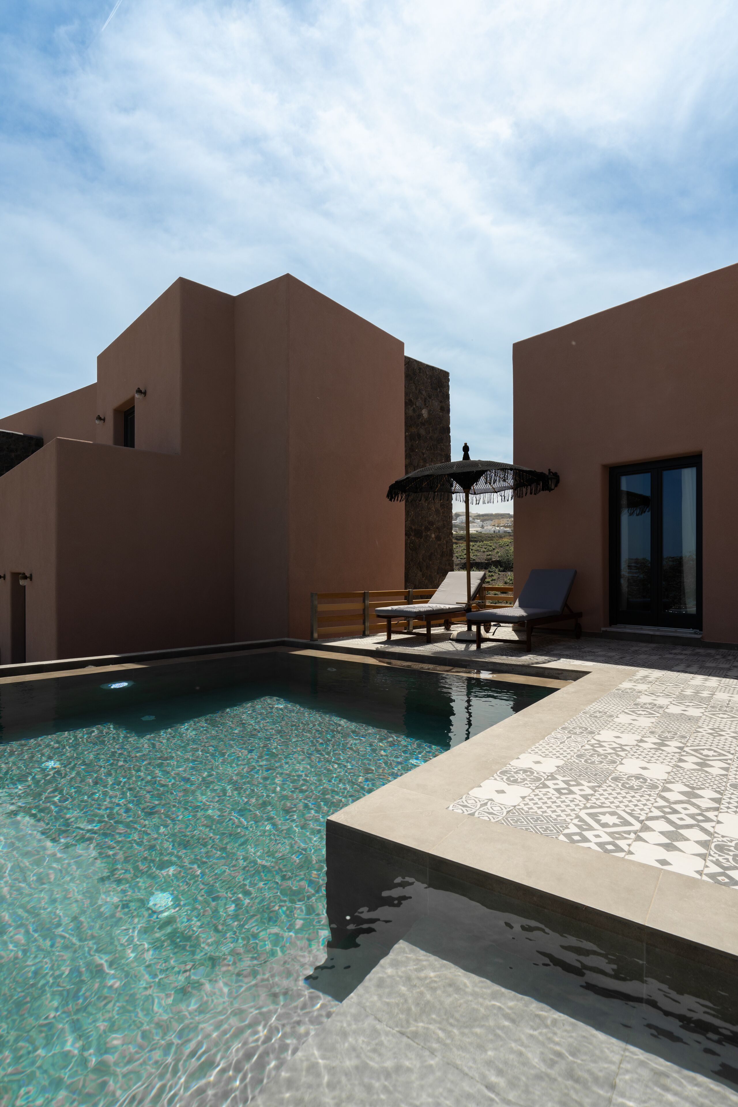 Une piscine entourée de chaises longues et agrémentée d’un parasol, le tout bordé par un bâtiment doté d’un mur en pierre.
