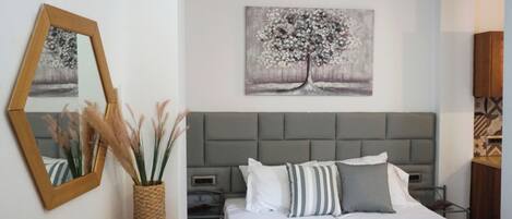 A neatly arranged bedroom with a bed, bedside tables, a mirror, and artwork on the wall.
