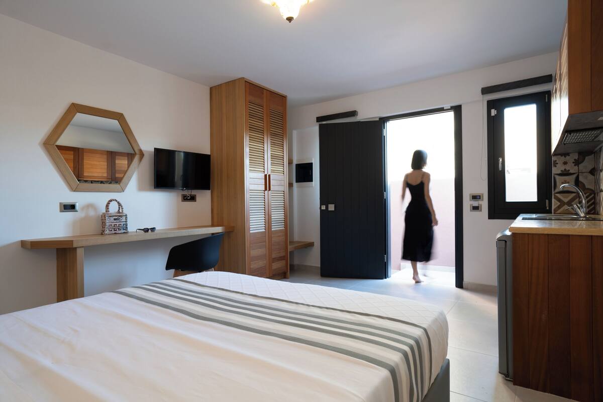 Quarto de hotel com cama, escrivaninha, televisão, guarda-roupa e banheiro.