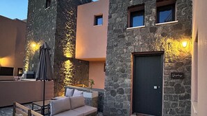 A courtyard with a stone building, a sofa, a bench, and patterned flooring. -  Golden Moments Luxury Stone Villas. (Santorini)