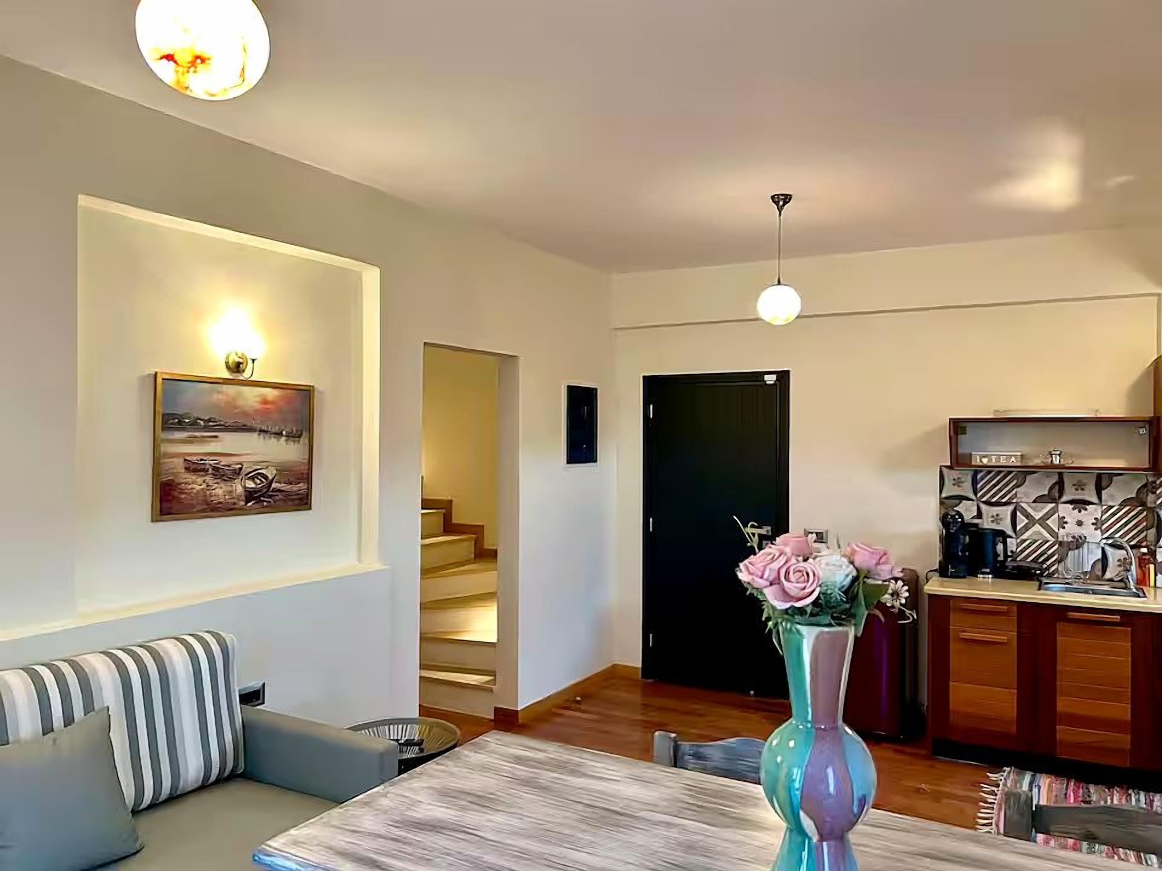 Ein Wohnzimmer mit einer Couch, einem Esstisch, einer Vase mit Blumen, einer Treppe und einer Küchenzeile.