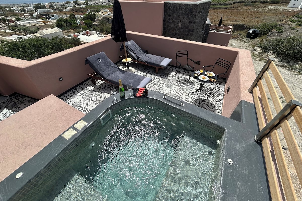Área de piscina no terraço com espreguiçadeiras e banheira de hidromassagem, em piso trabalhado e com vista para a paisagem.