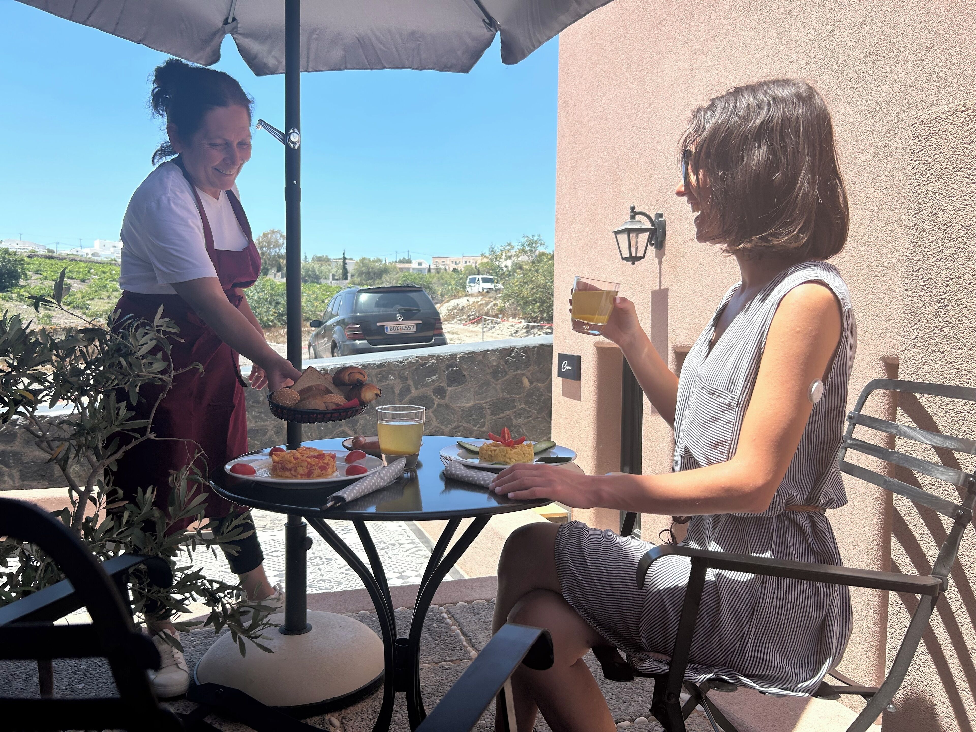 An outdoor dining area with a table set for two, a basket of bread, and a glass of drink.