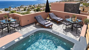 A rooftop pool area with lounge chairs, a table, and a view of the sea.