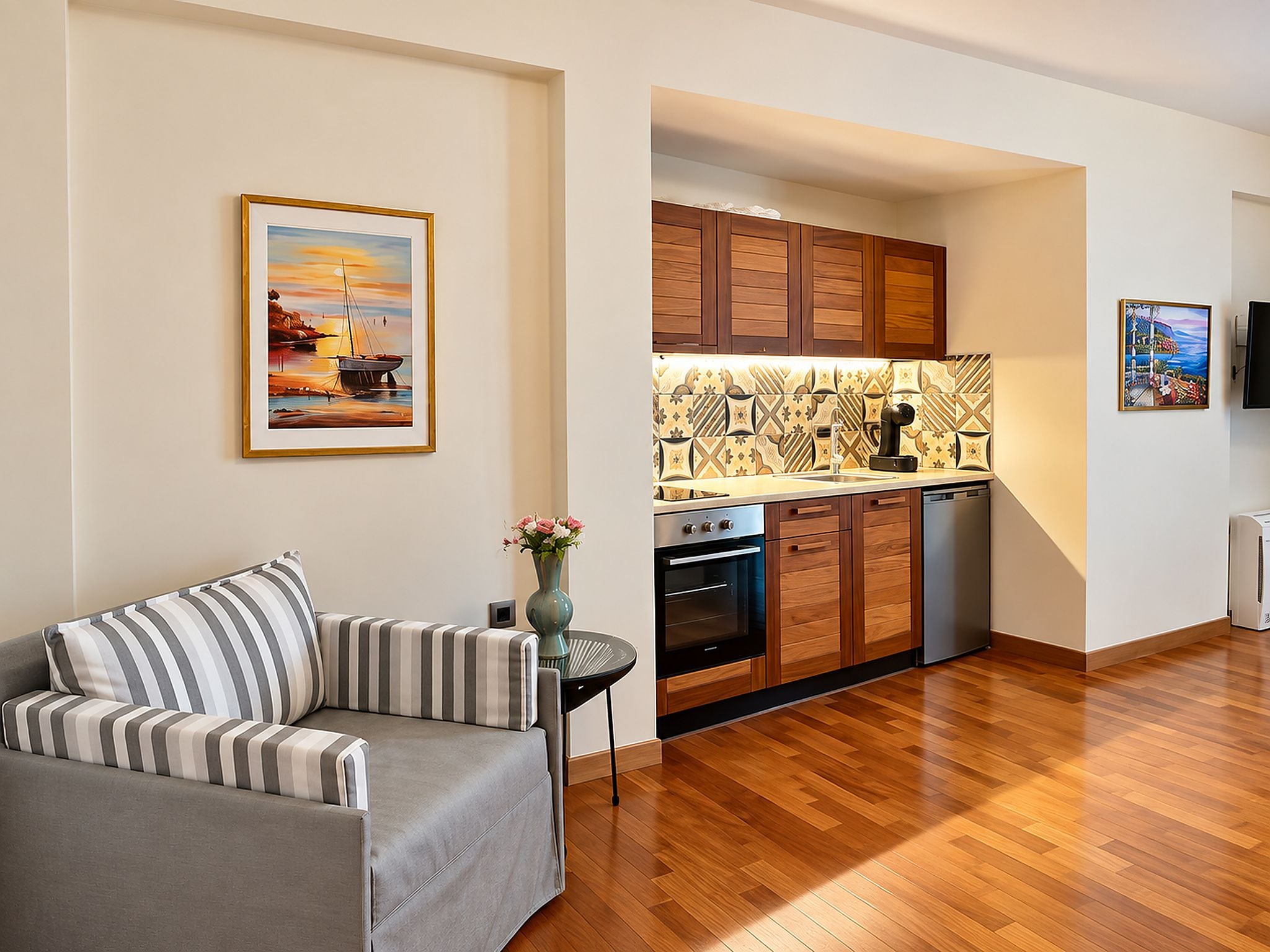 A modern living room with a sofa, a small table with a vase, and a kitchen with wooden cabinets and a tiled backsplash.