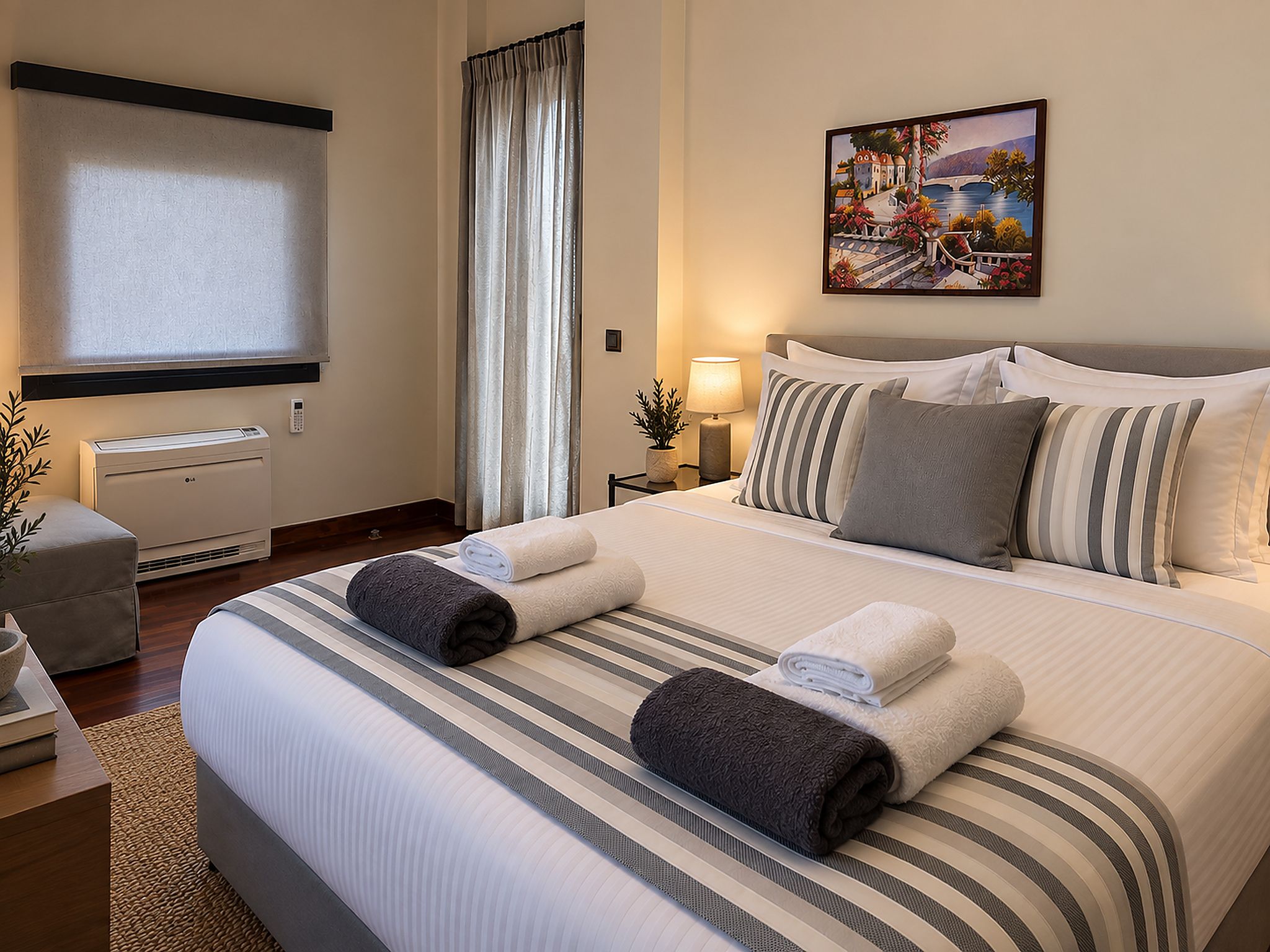 A hotel room with a large bed, a bedside table with a lamp, a window with curtains, and a painting on the wall.