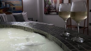 A room with a hot tub, two glasses of white wine, and artwork on the walls. -  Golden Moments Luxury Stone Villas. (Santorini)