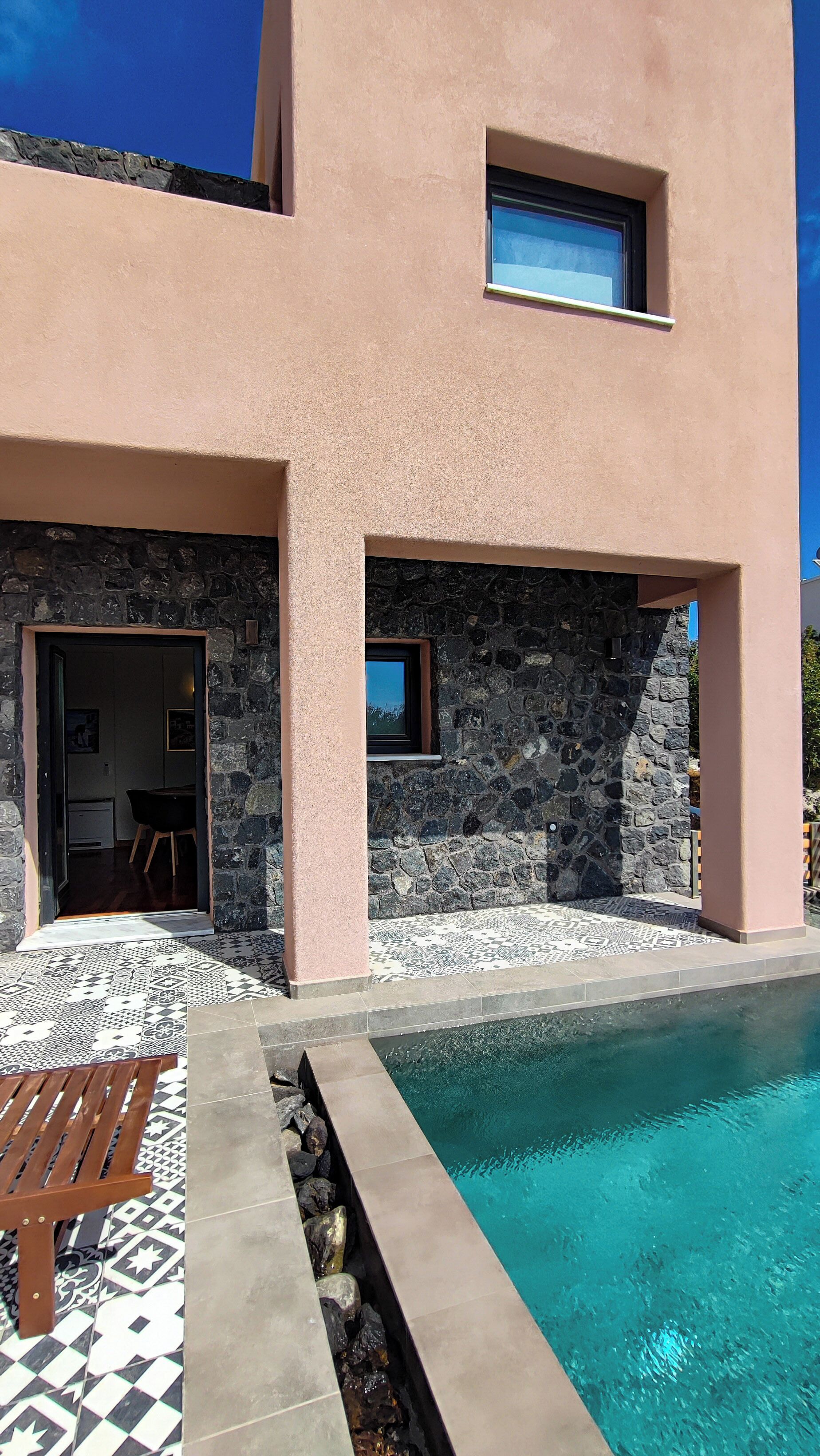A modern building with a swimming pool, stone walls, and a tiled patio area.