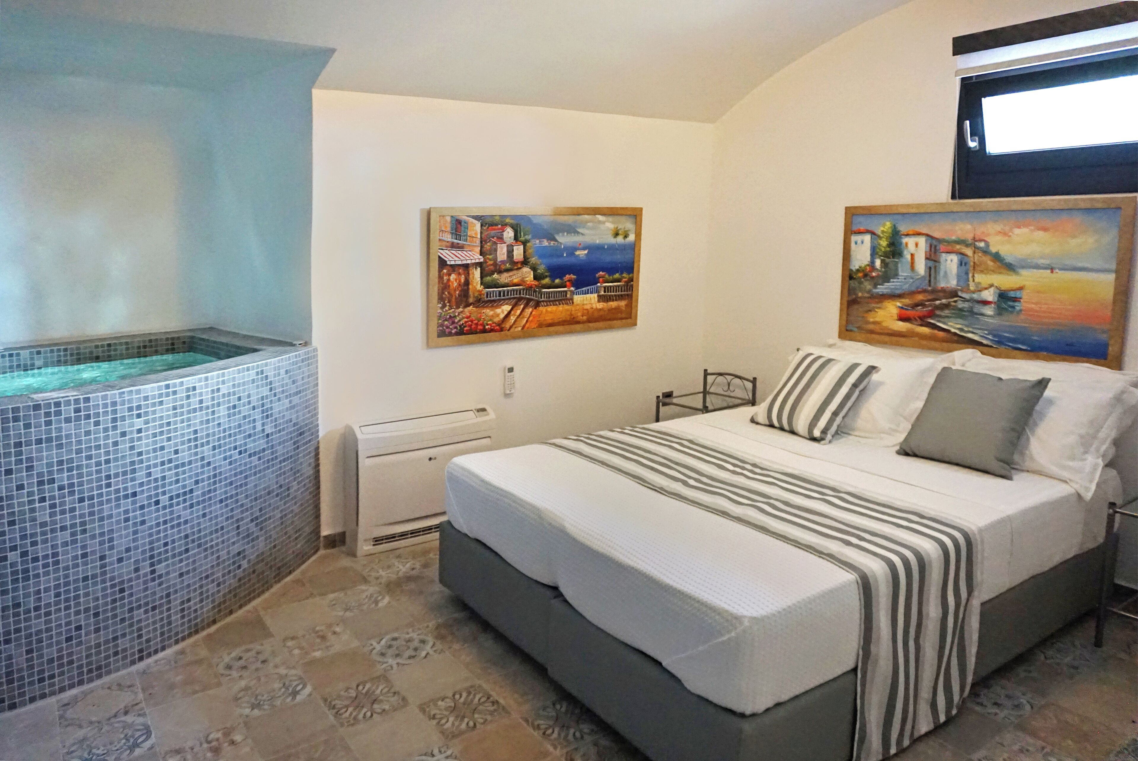 Ein Schlafzimmer mit einem Bett, einem kleinen Fenster, einem Wandheizkörper und einer gefliesten Badewanne.