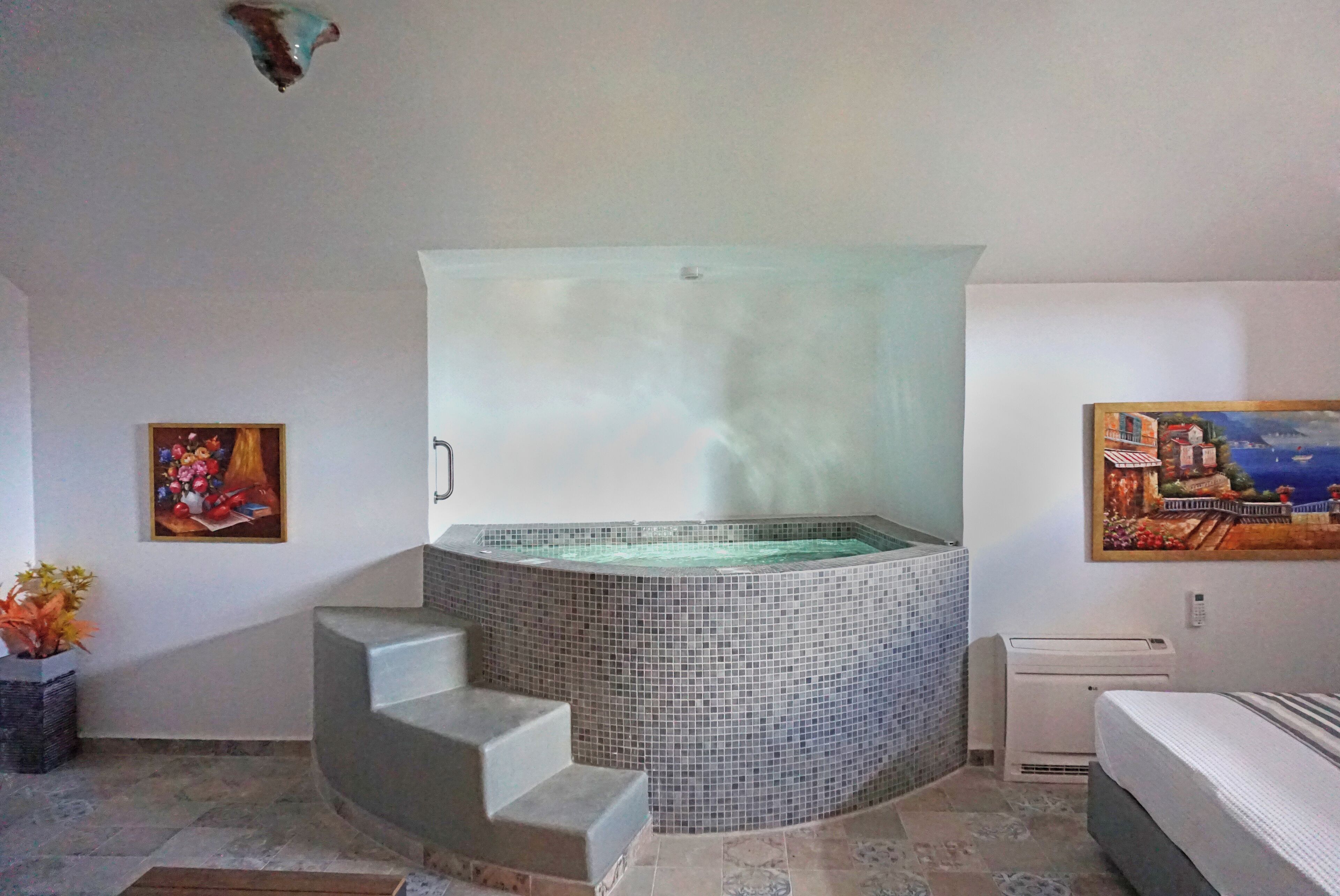 Une salle de bain avec un jacuzzi orné de mosaïques, un tableau et une plante en pot.