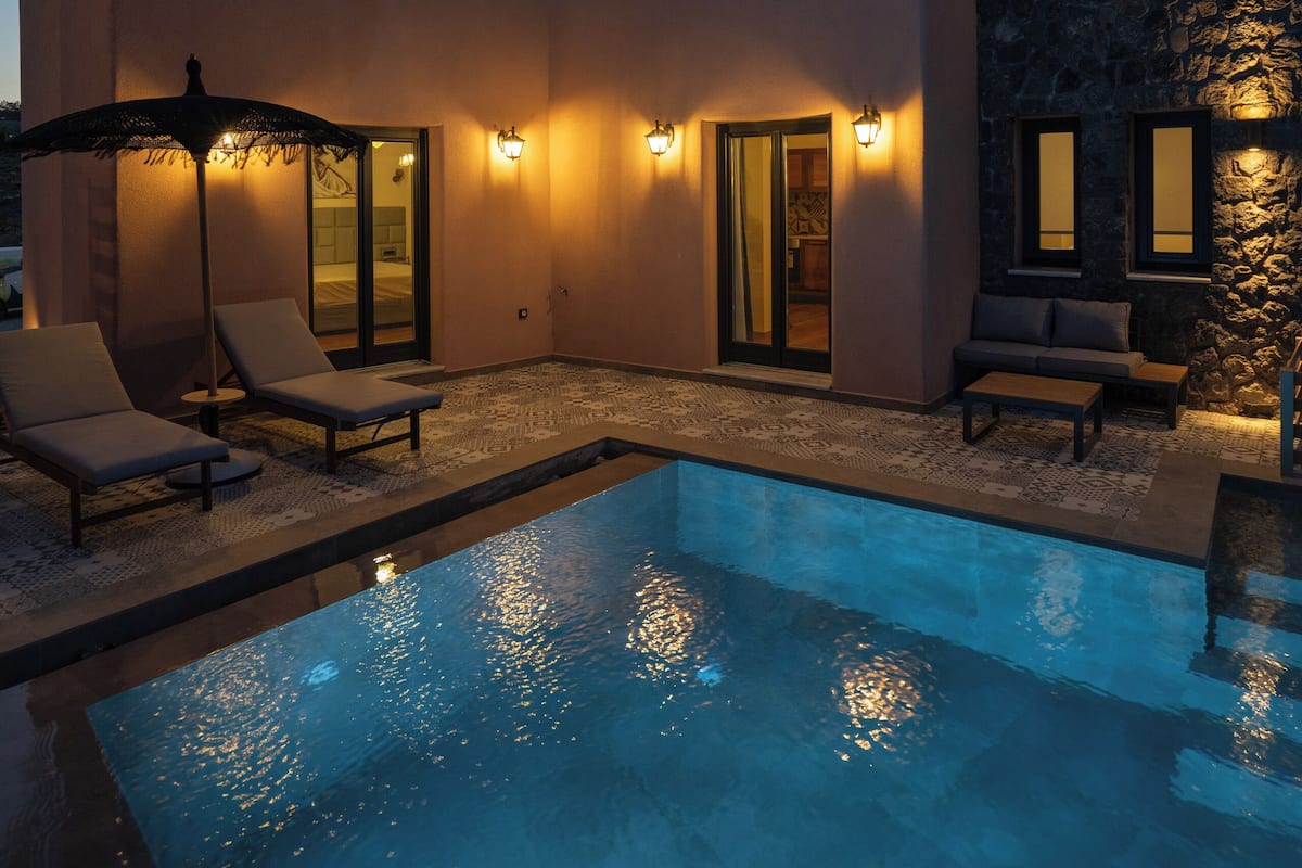 Uma casa moderna com piscina, cadeiras de descanso e uma parede de pedra.