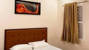 A hotel room with a bed, a ceiling fan, an air conditioning unit, a window with curtains, and a painting on the wall. - Izi Airport Stay (Chennai)