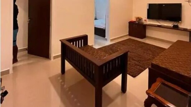 A modern living room with a TV, a sofa, and a dining table. - Izi Airport Stay (Chennai)