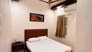 A bedroom with a bed, a nightstand, a ceiling fan, an air conditioning unit, and a window with curtains. - Izi Airport Stay (Chennai)