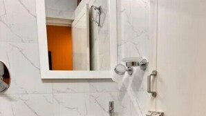 A bathroom with a white sink, a mirror, and a black trash bin. - Izi Airport Stay (Chennai)