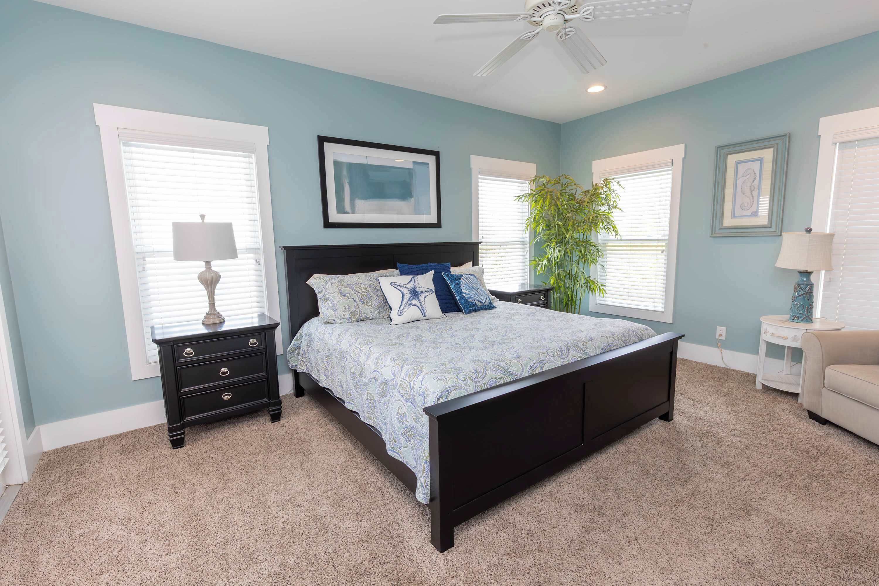 A bedroom with a bed, a nightstand, a lamp, a ceiling fan, and a window with blinds.