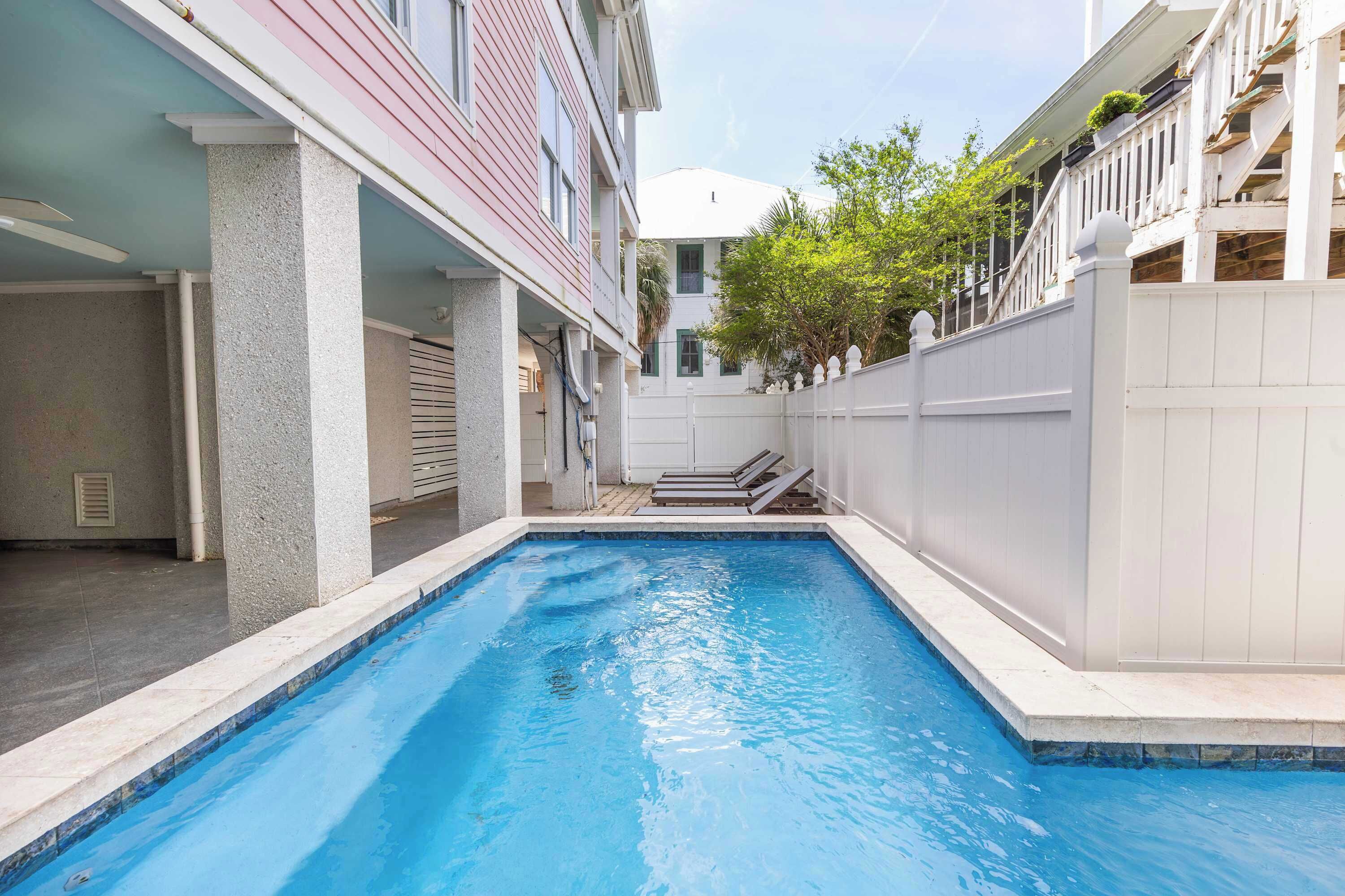 A swimming pool with a white fence, a building with a balcony, and a clear sky.