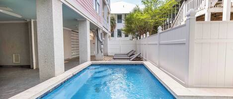A swimming pool with a white fence, a building with a balcony, and a clear sky.