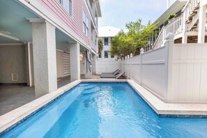 A swimming pool with a white fence, a building with a balcony, and a clear sky. - Game Room and Private Heated Pool + 5BR Sleeps 12 (Tybee Island)