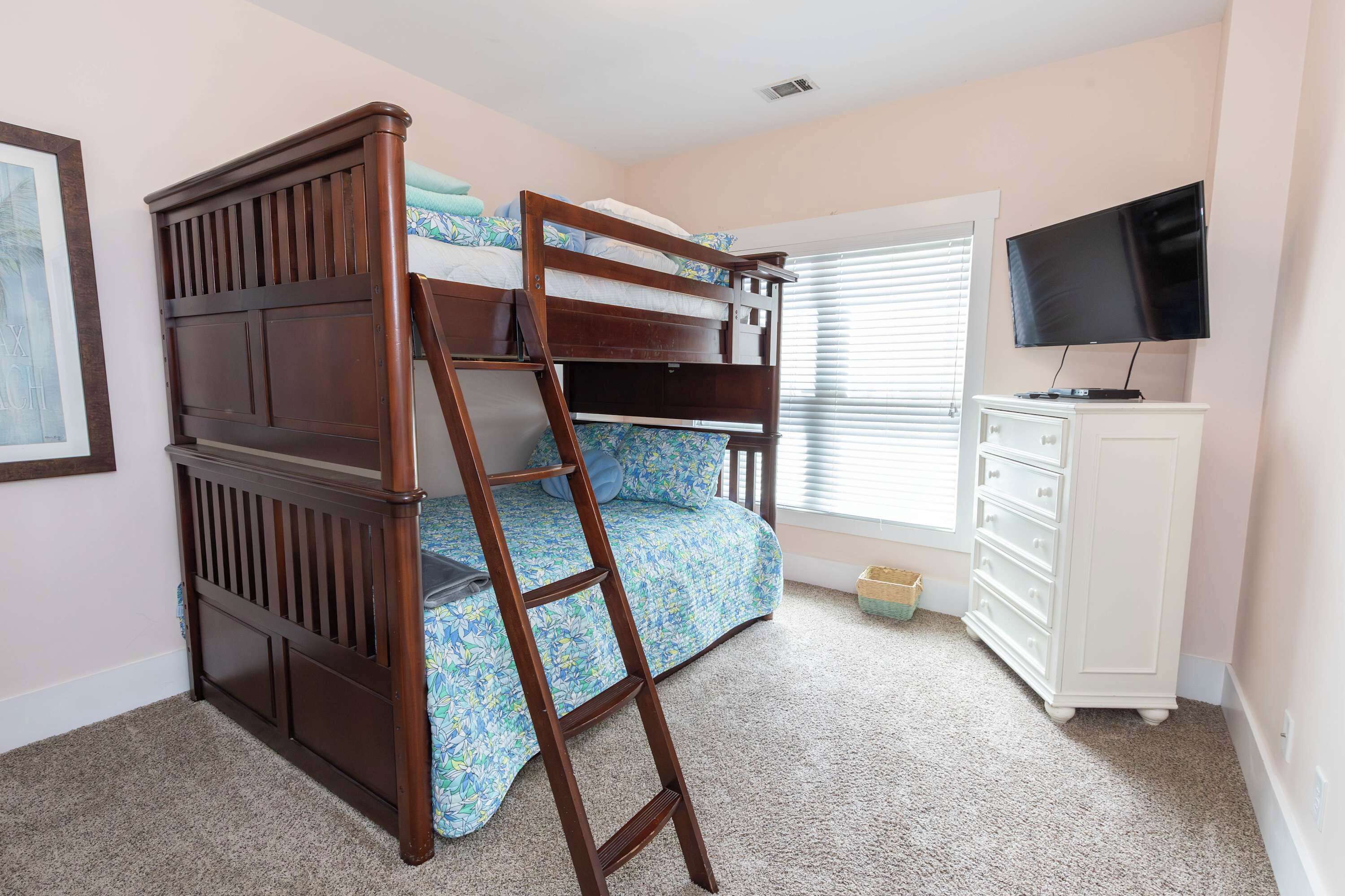 A bunk bed with a wooden ladder, a television on a stand, and a window with blinds.