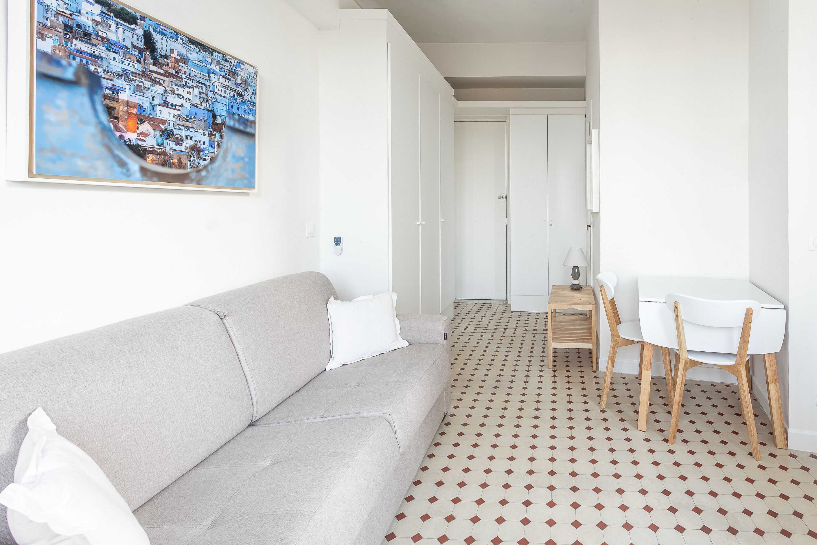 A modern living room with a grey sofa, white chairs, a small wooden table, and a patterned floor.