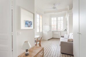 A modern, white-themed room with a dining area, a sofa, and a kitchen visible through an open door.