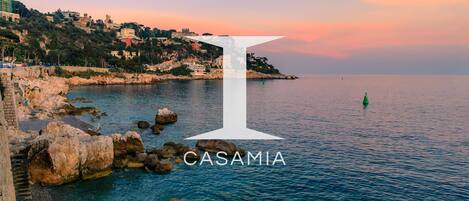 A coastal view with a prominent white 'I' symbol and the word 'CASAMIA' indicating a location.