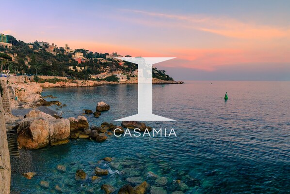 A coastal view with a prominent white 'I' symbol and the word 'CASAMIA' indicating a location.