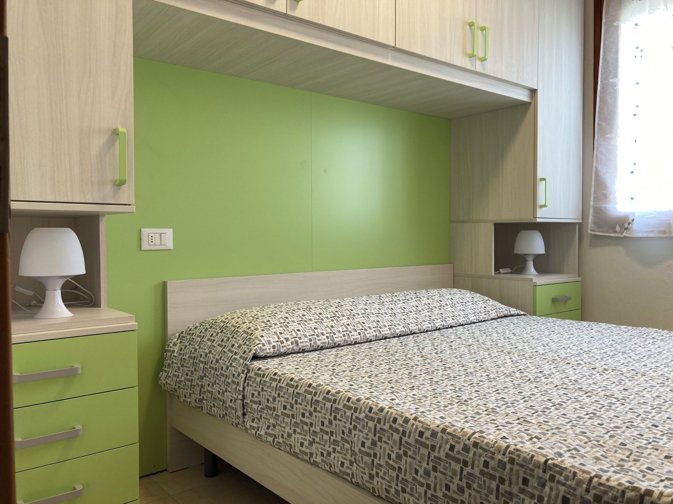 A bedroom with a bed, a nightstand, a lamp, and a dresser.