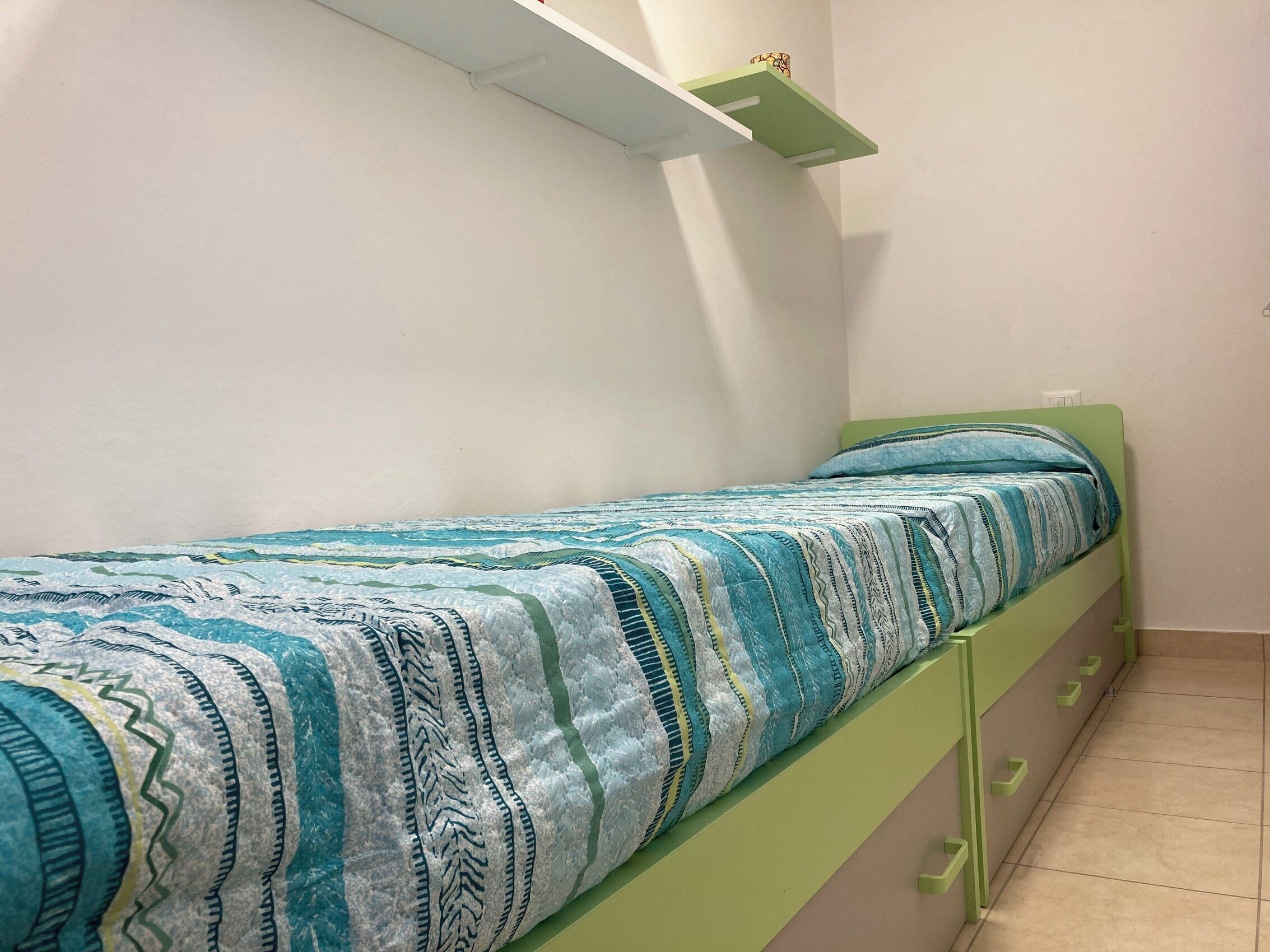 Uma cama de solteiro com um cobreleira estampada, cabeceira verde e parede branca.