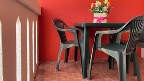 Un petit espace extérieur aménagé pour prendre les repas, avec un mur rouge, une table et deux chaises.