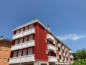 Ein mehrstöckiges Wohngebäude mit Balkonen, einer roten Fassade und blauem Himmel.