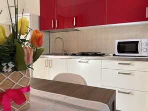 A modern kitchen with red cabinets, a white countertop, a microwave, and a sink. - Lovely Flat in the Center of Rosolina Mare (Rosolina)