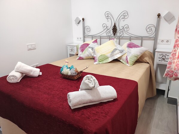 A neatly made bed with a red blanket, two rolled towels, and a basket of folded towels. - Cerca de la Playa,centro y Estación de Tren. Casa de 2 Plantas en Barrio Seguro (Málaga)