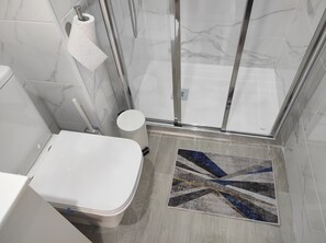 A bathroom with a toilet, a shower with a glass door, and a patterned rug on the floor. - Cerca de la Playa,centro y Estación de Tren. Casa de 2 Plantas en Barrio Seguro (Málaga)