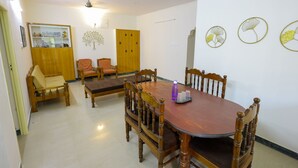 A dining area with a wooden table and chairs, a ceiling fan, and a wall with decorative leaf patterns. - Izi Transit Stay (Chennai)