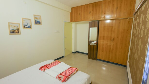 A bedroom with a bed, wooden wardrobe, and three wall-mounted pictures. - Izi Transit Stay (Chennai)