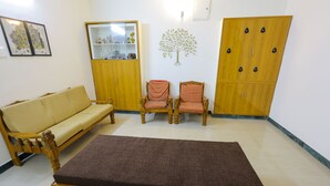 A living room with a sofa, two patterned chairs, a cabinet, and a large wooden wardrobe. - Izi Transit Stay (Chennai)