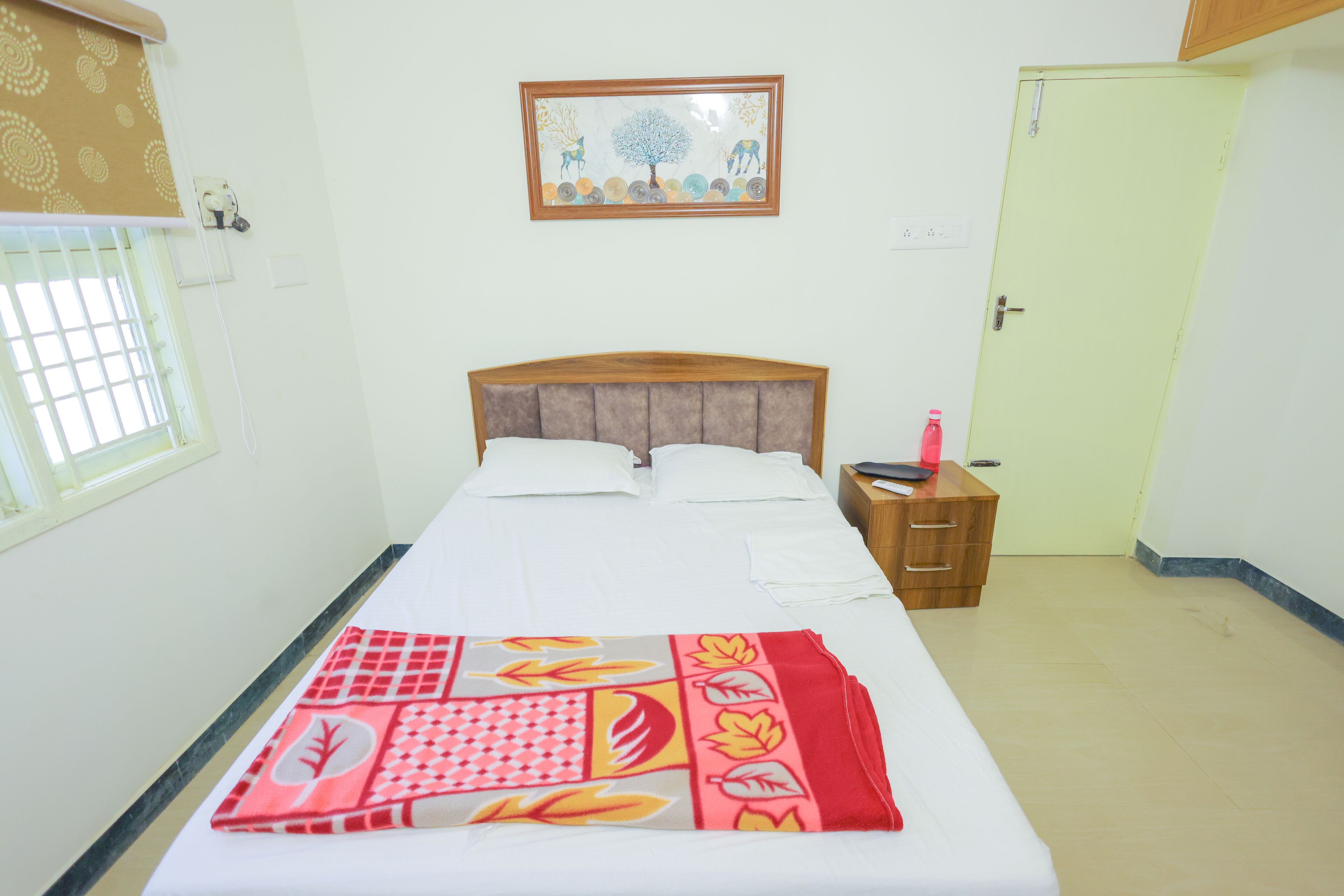 Cama bem arrumada com um edredom estampado, mesa de cabeceira com uma garrafa e um quadro na parede.