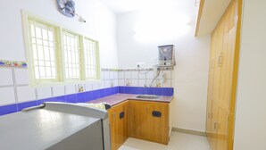 A kitchen with wooden cabinets, a sink, and a window with a grid pattern. - Izi Transit Stay (Chennai)