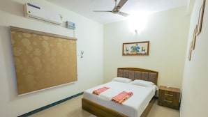 A bedroom with a bed, a ceiling fan, an air conditioning unit, a nightstand, and a framed picture on the wall. - Izi Transit Stay (Chennai)