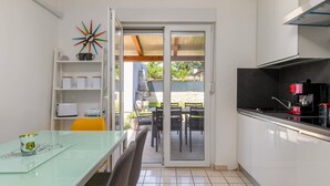 Uma cozinha moderna com armários brancos, uma mesa de jantar de vidro e uma porta de correr que dá para uma área externa.