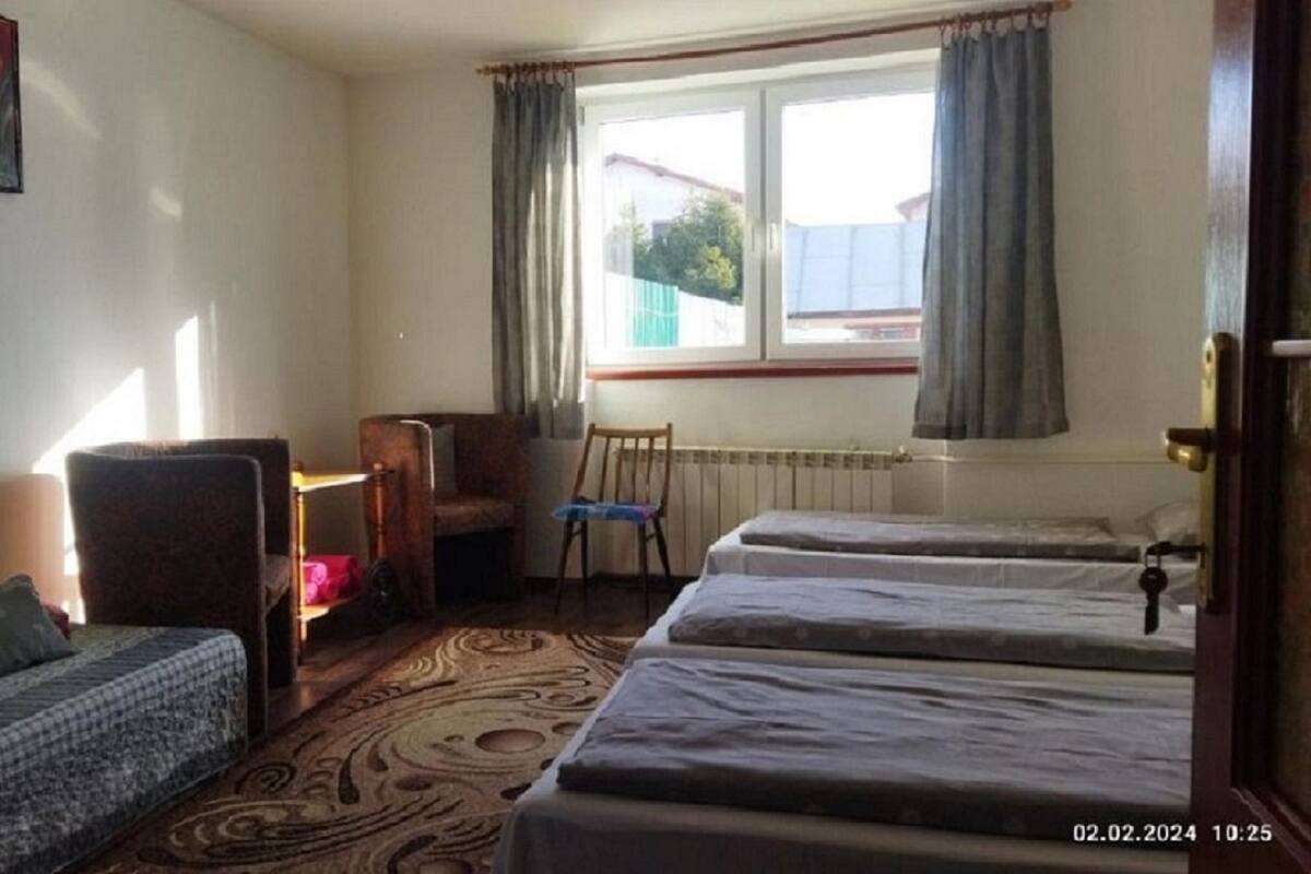 A hotel room with two single beds, a sofa, a chair, a small table, and a window with curtains.