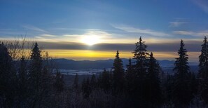 A mountainous landscape with evergreen trees and a sunset in the background. - Lucky Cat  (Nova Lesna)