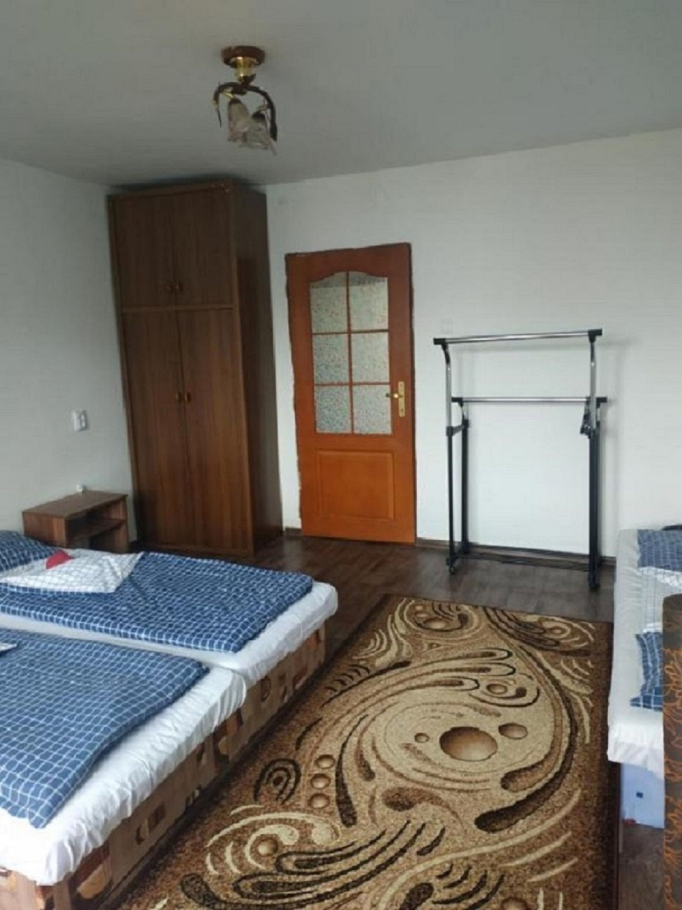 Quarto com duas camas, um guarda-roupa, uma porta com janela e um ventilador de teto.